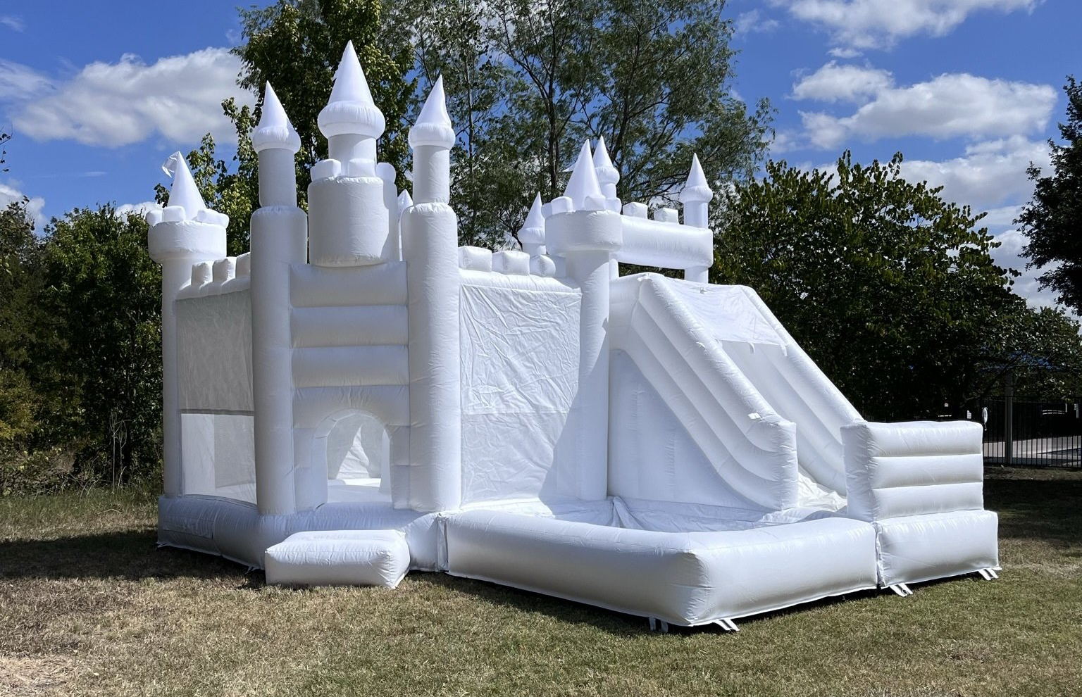 A white bouncy castle with a slide is sitting in a grassy field.