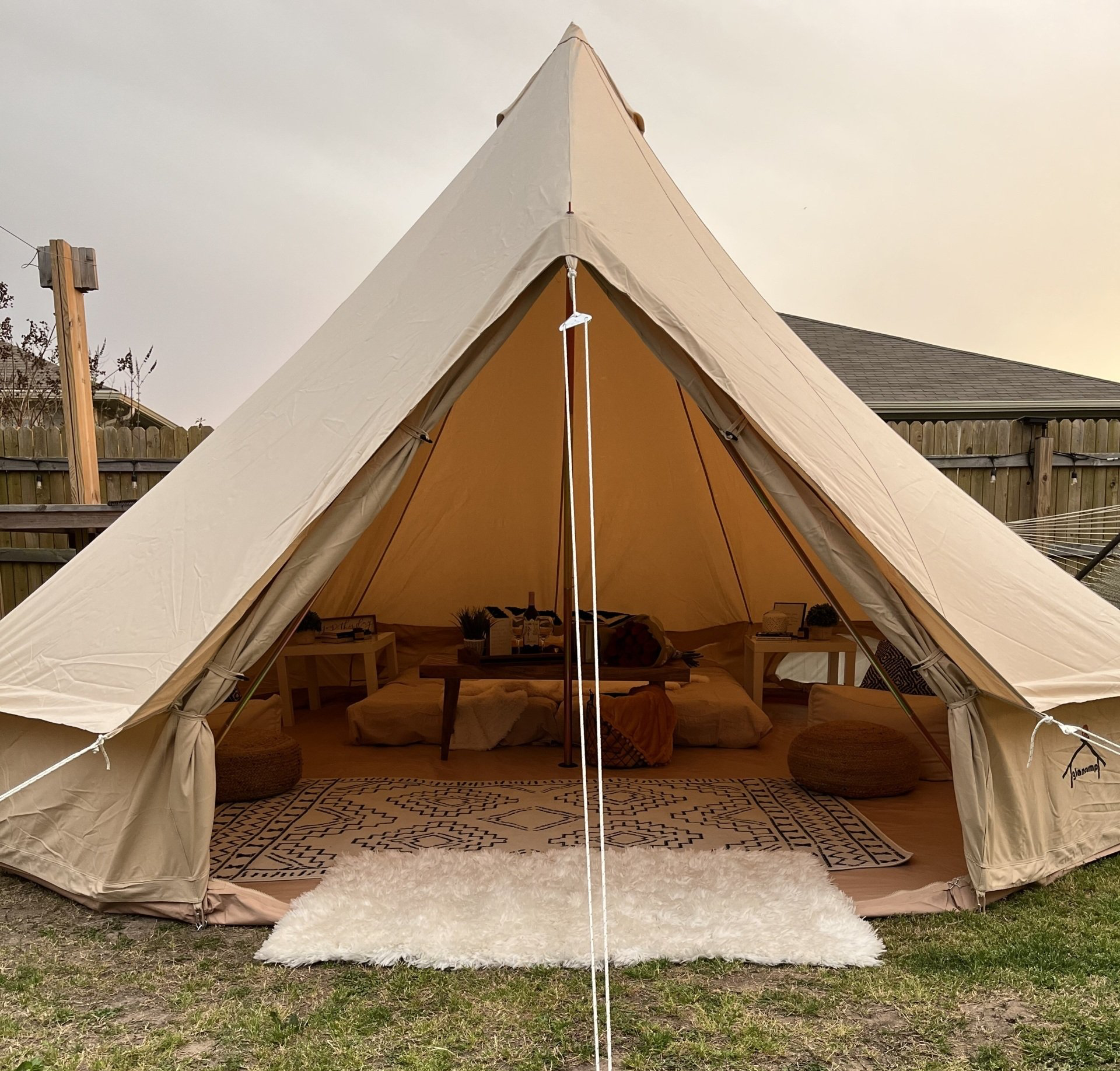 A large tent is sitting in the grass in front of a house.