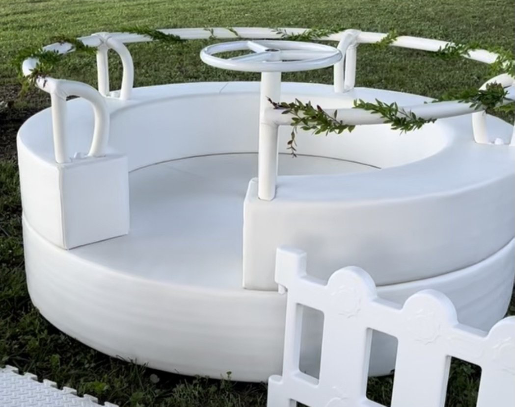 A white merry go round is sitting in the grass next to a white fence.