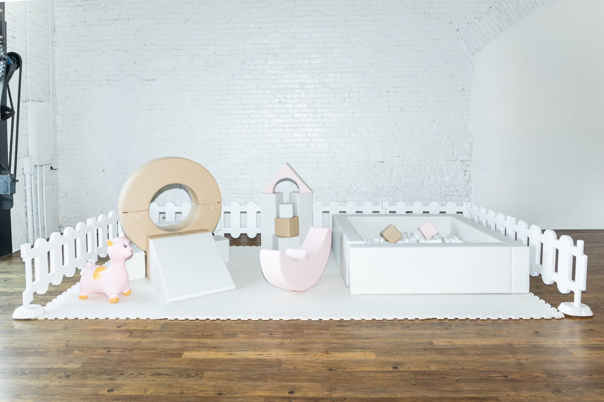 A room with a wooden floor , white fence , and toys on the floor.