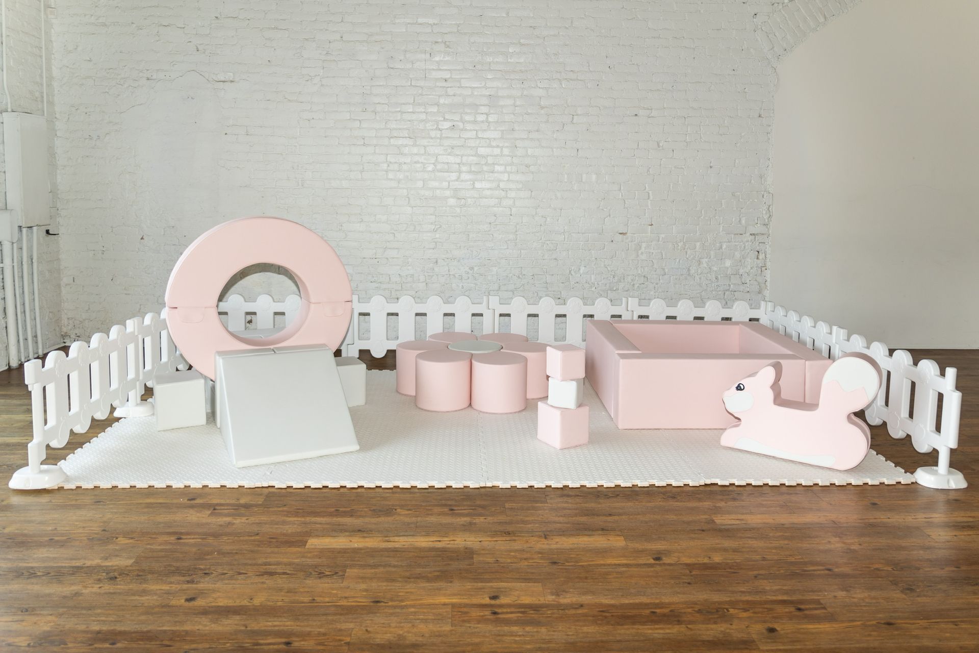 A room with a white fence and pink and white toys on the floor.