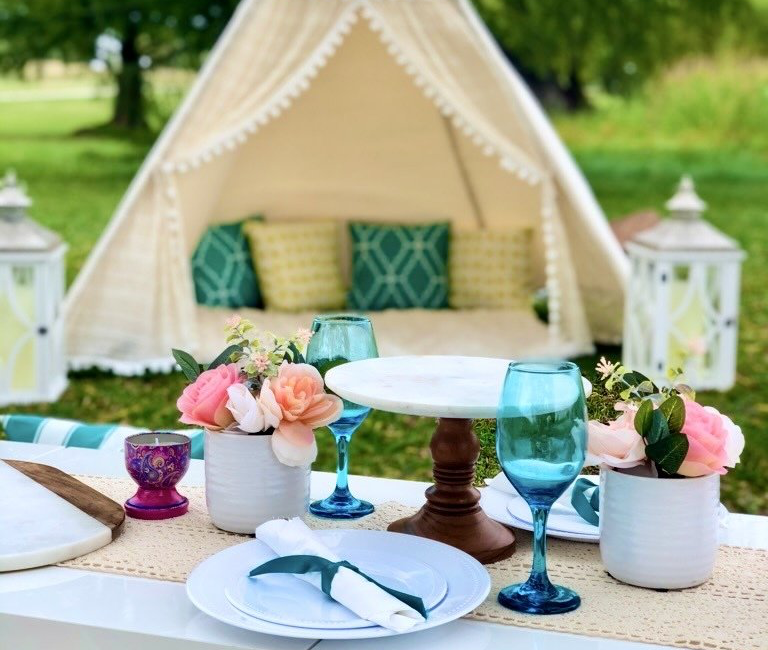 A table with plates , glasses , and flowers in front of a tent.