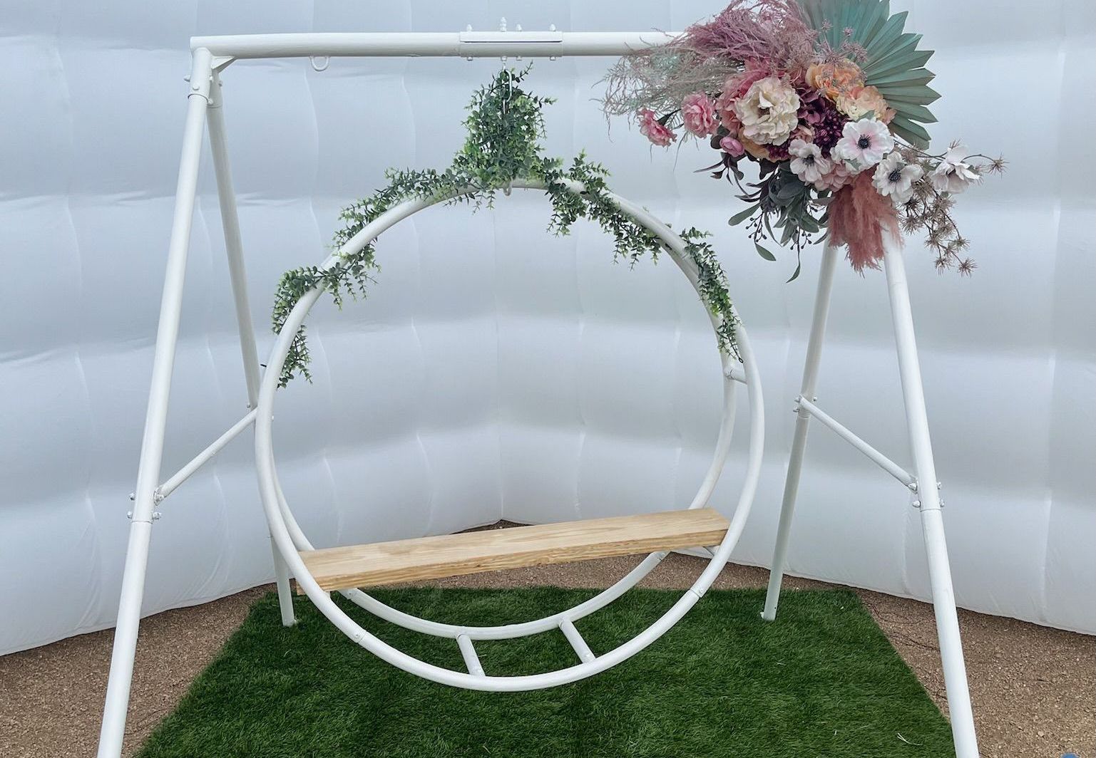 A white swing with flowers on it is sitting on top of a lush green field.