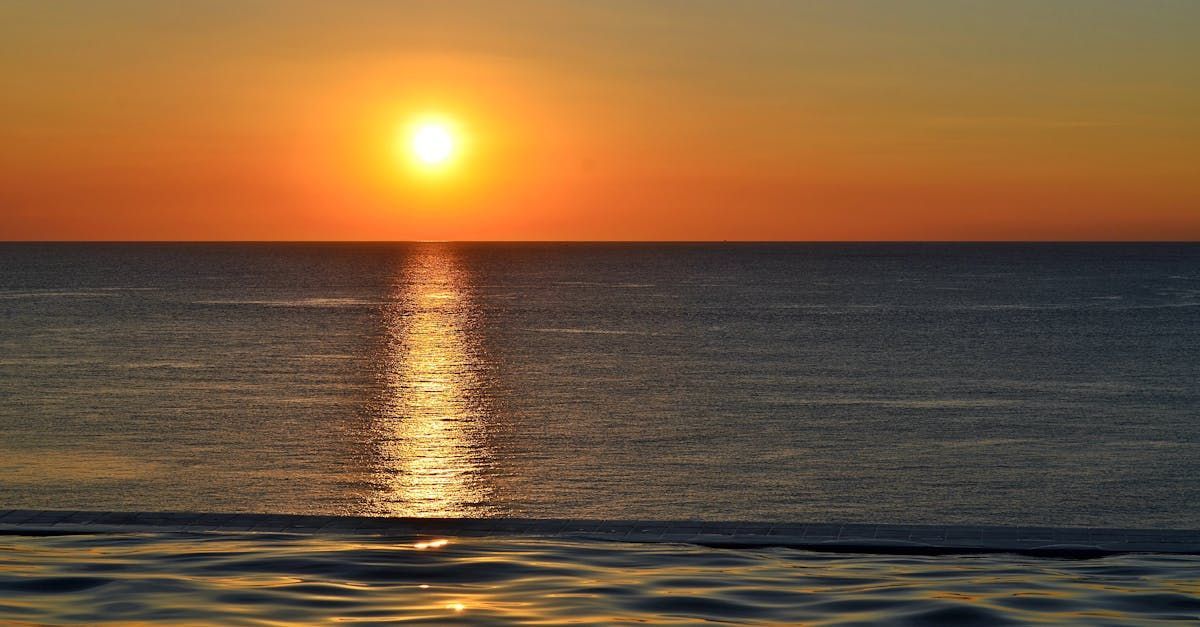 Zonsondergang boven de kalme oceaan; de weerspiegeling van de zon schittert op het water, in oranje en gouden tinten.