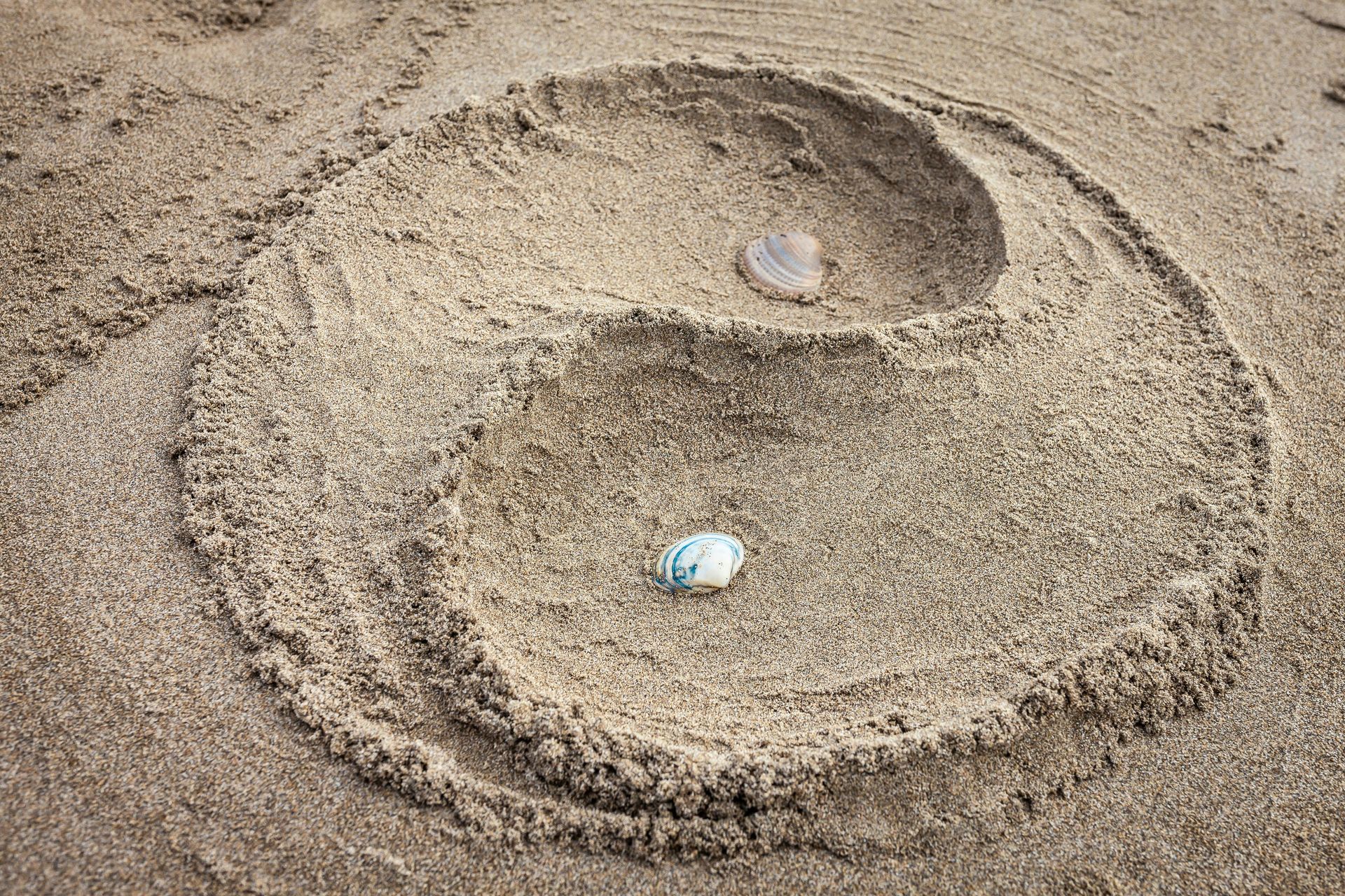 Yin Yang-symbool getekend in zand met twee schelpen.
