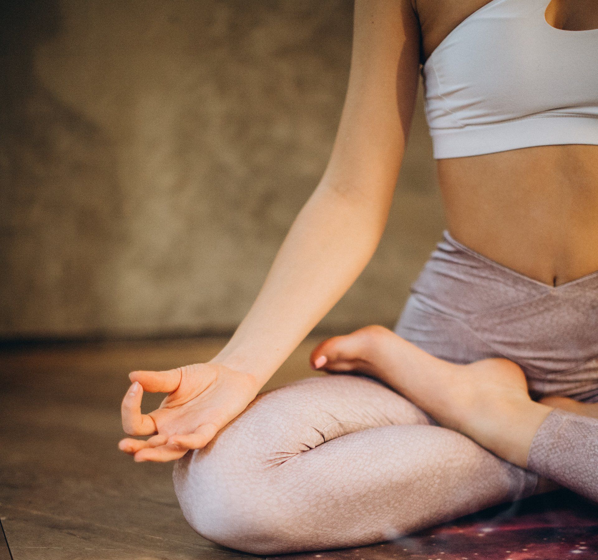 Vrouw in yogahouding, handen in mudra, gekleed in een wit topje en roze legging, binnenshuis.