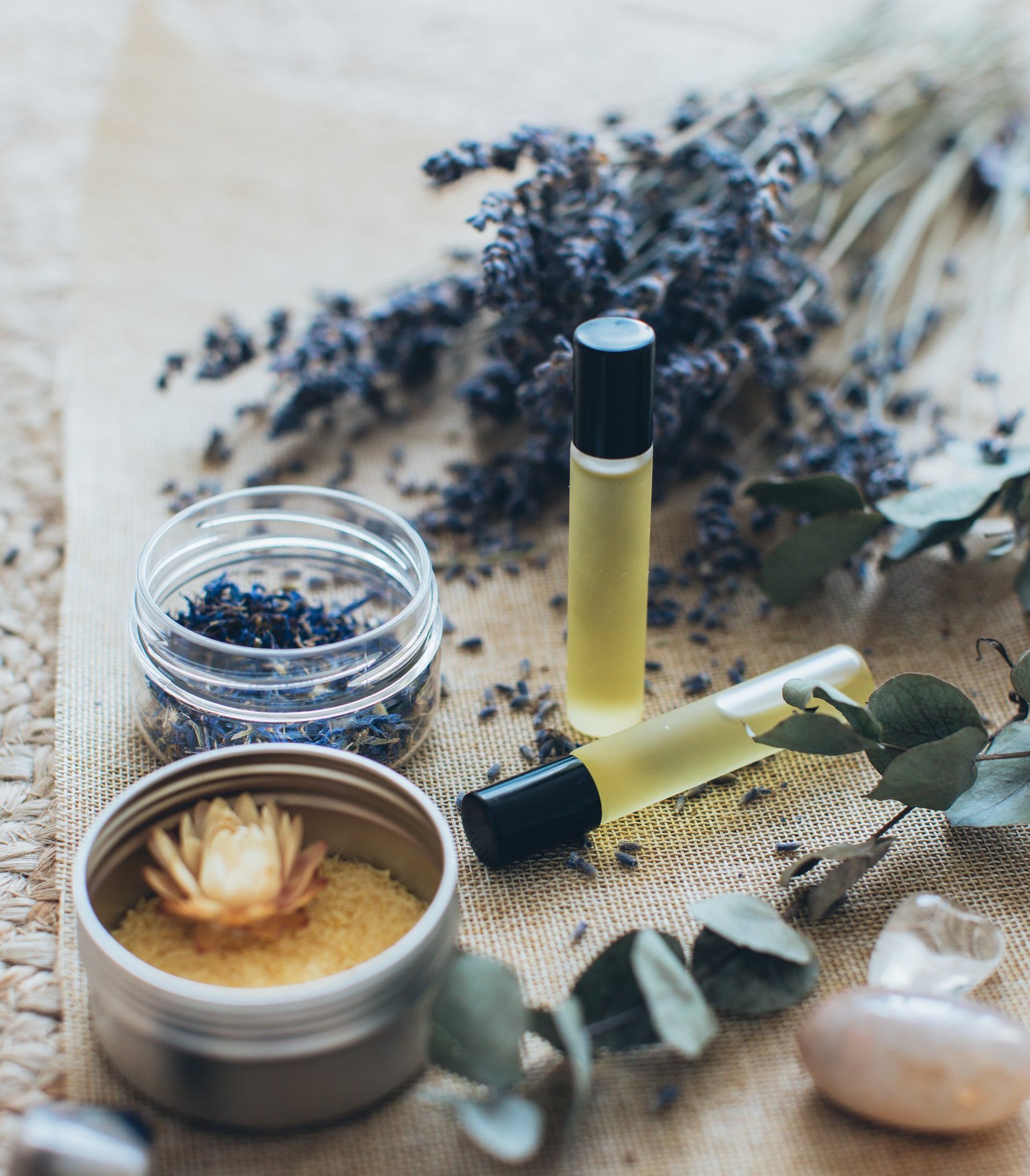 Lavendel, etherische olierollers, gedroogde bloemen en kristallen op een rustieke doek.