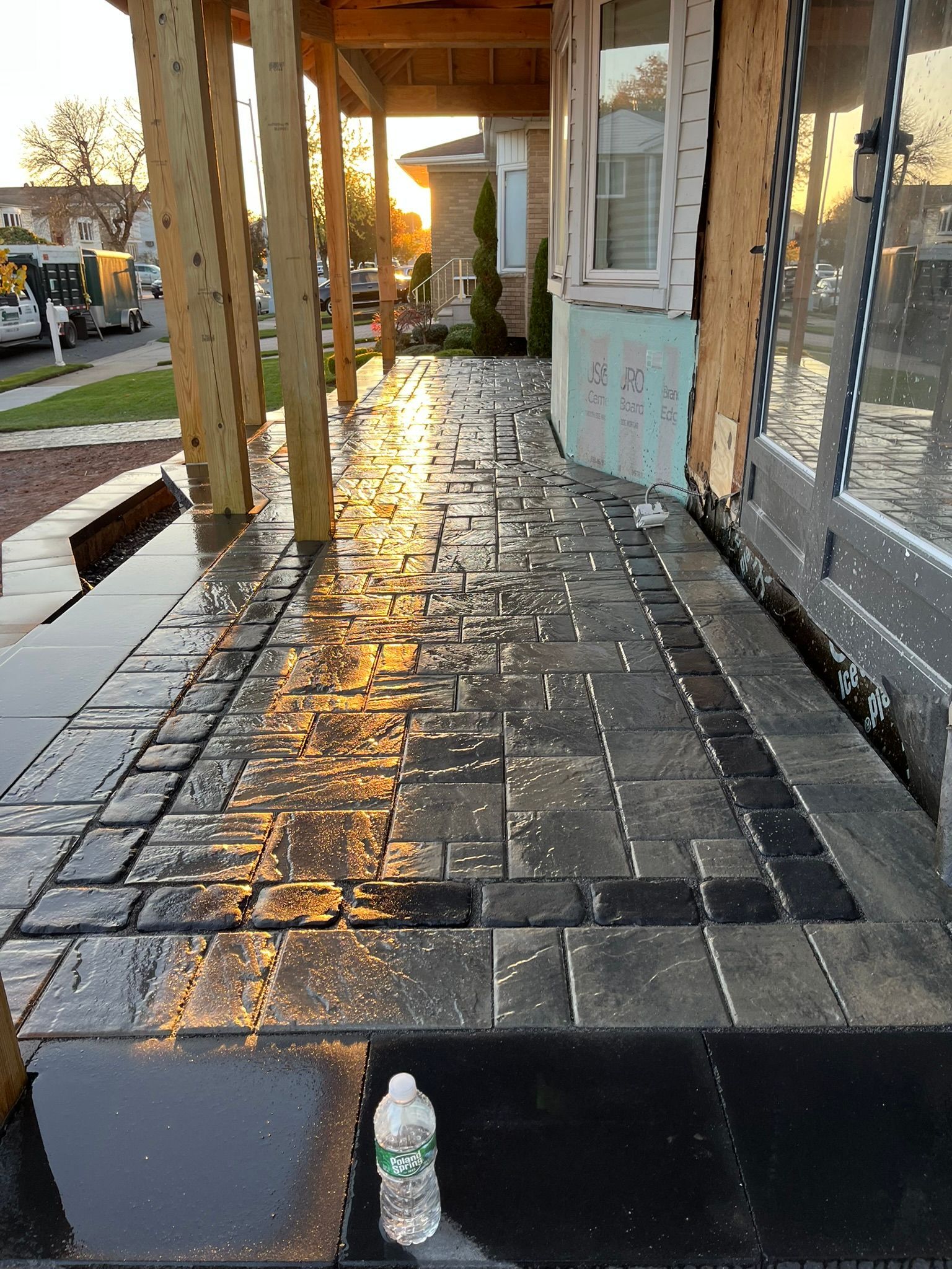 A bottle of water is sitting on the sidewalk in front of a house under construction.
