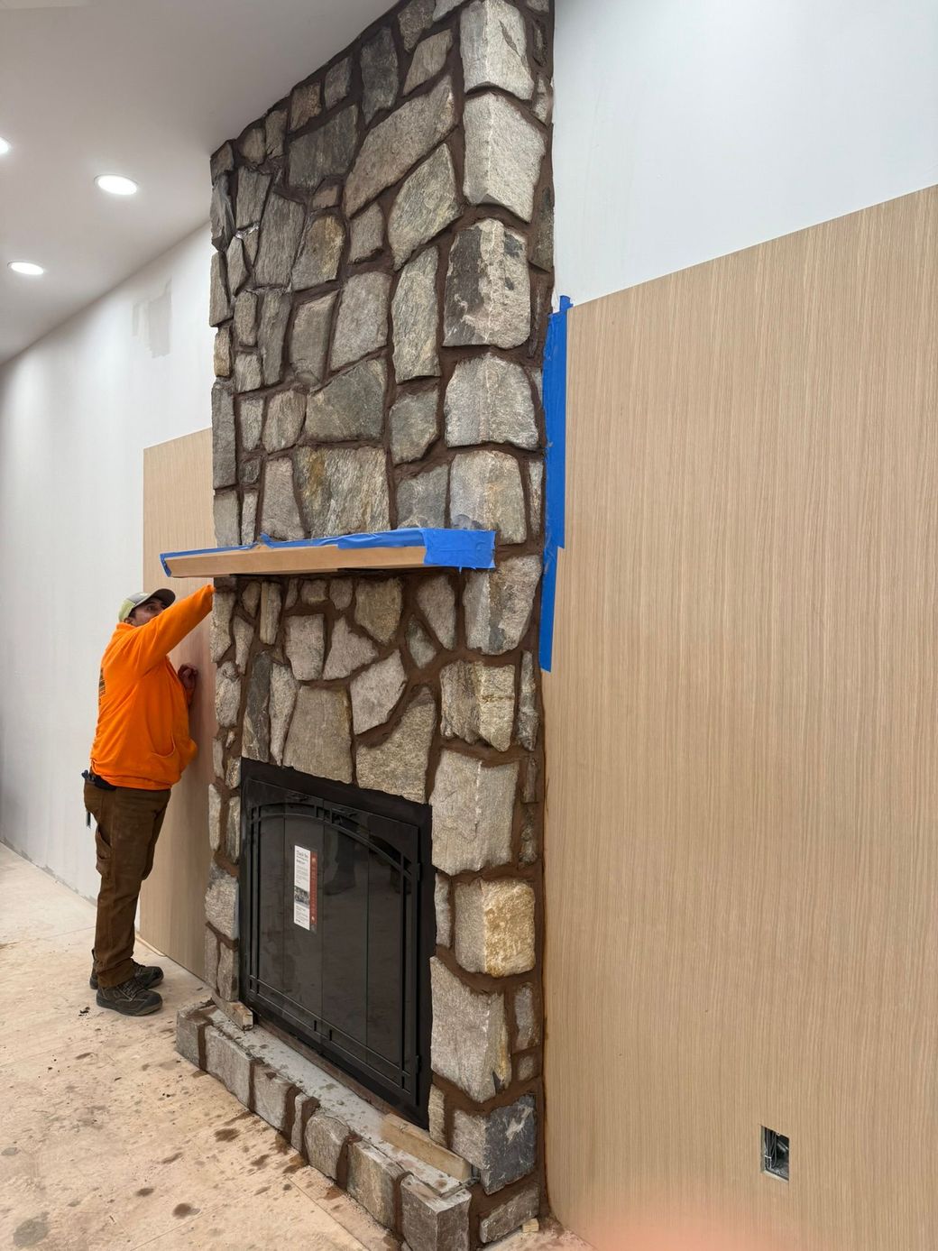 A man is working on a stone fireplace in a living room.
