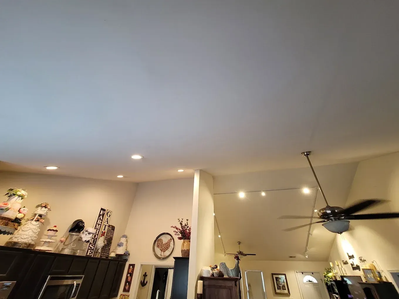 High ceiling in a room with a ceiling fan, lights, and decorated cabinets.