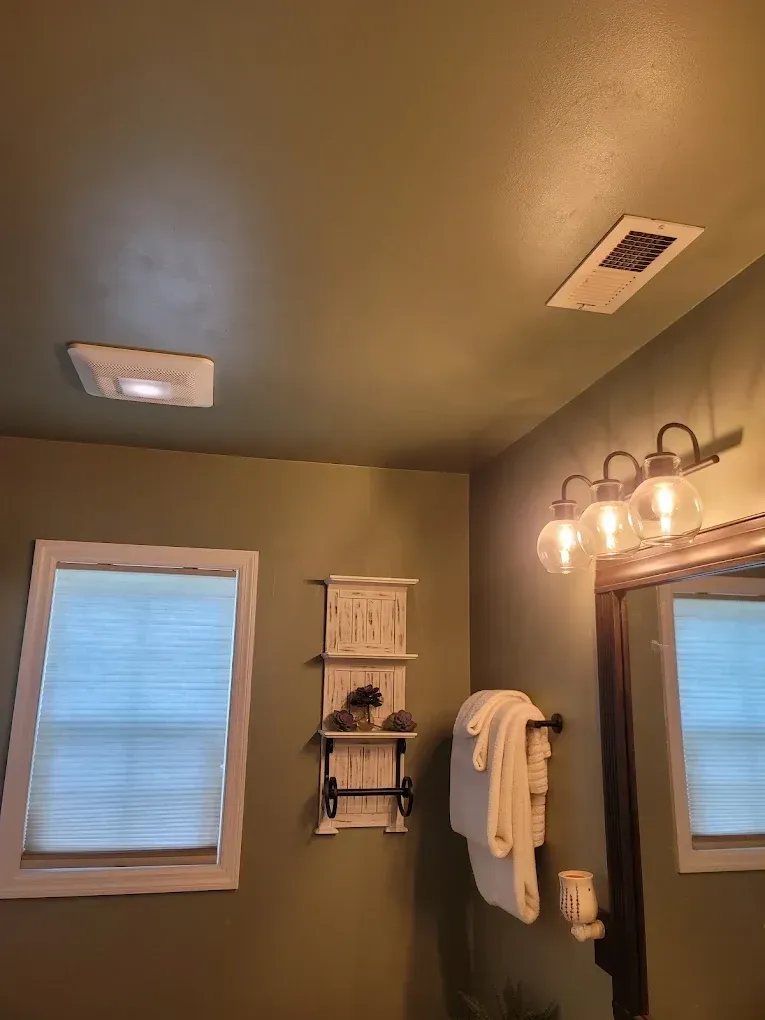 Bathroom with green walls, two ceiling lights, vanity mirror, and window with blinds.