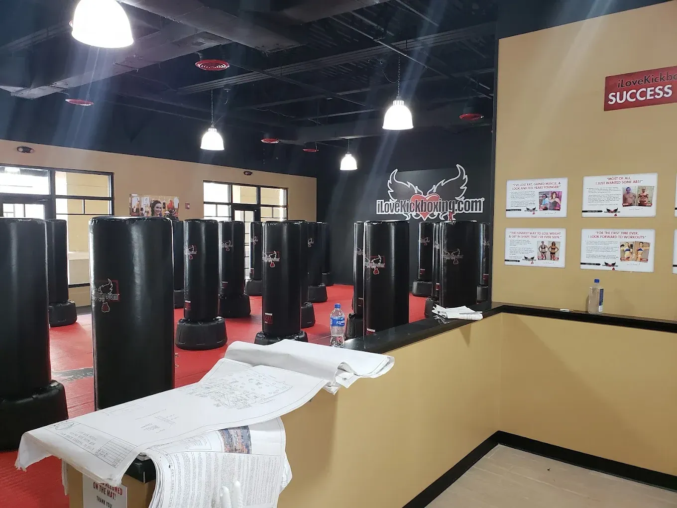 Interior of a kickboxing gym with black punching bags, red floor, and beige walls.
