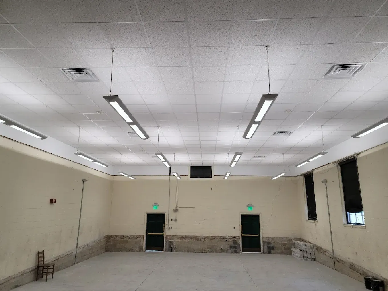 Empty room with white ceiling, fluorescent lights, two green doors, and beige walls.