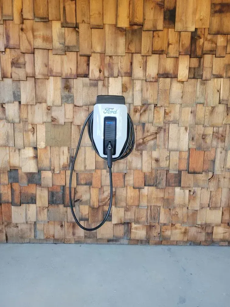 Ford electric vehicle charger on a wooden, textured wall. Cable hanging. Concrete floor.