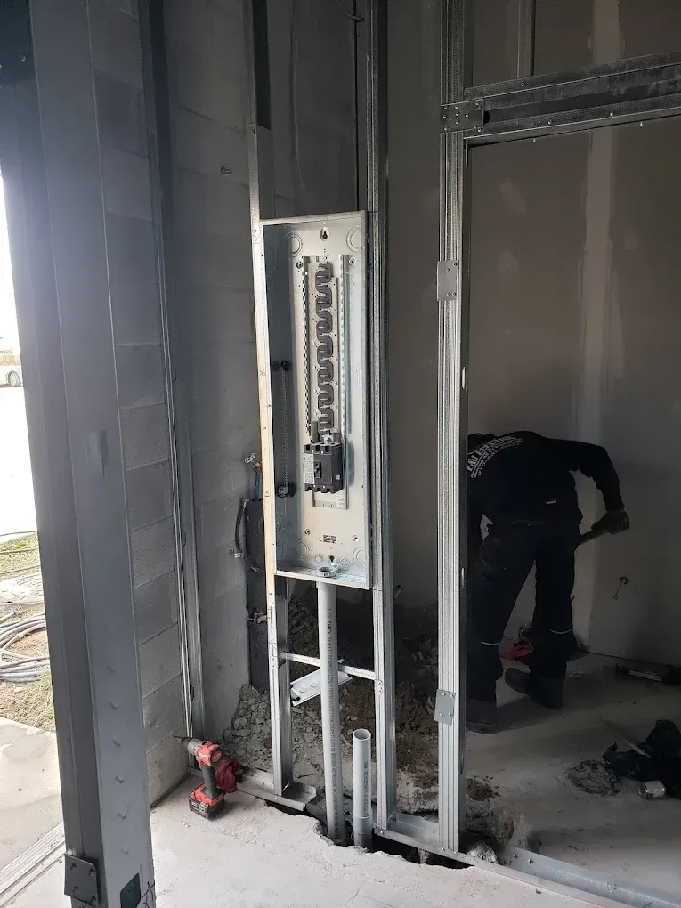 Electrical panel in a building under construction. A worker is in the doorway area.