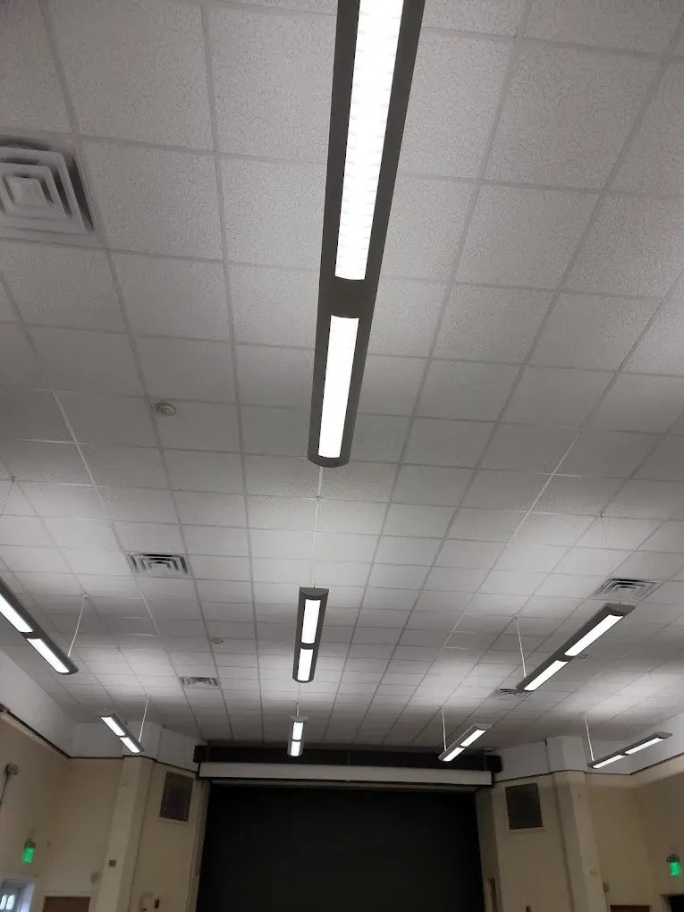 Fluorescent lights on a white grid ceiling in a room with a dark stage.