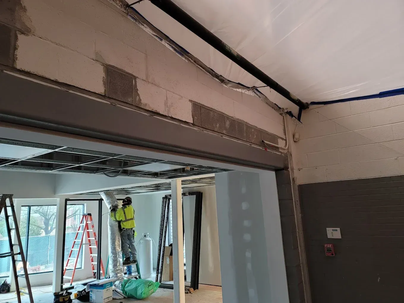 Construction site interior: workers, drywall, exposed wiring, and framing, with open doorway and ladders.