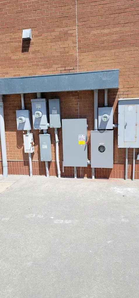 Electrical boxes mounted on a brick wall, with conduits running down to the ground.
