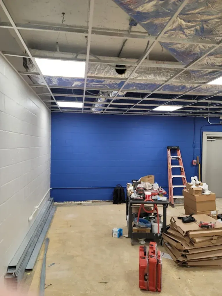 Construction site: room with blue and white walls, unfinished ceiling, tools, and a ladder.
