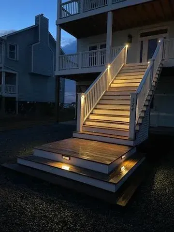Wooden stairs with built-in lights leading up to a two-story house at dusk.