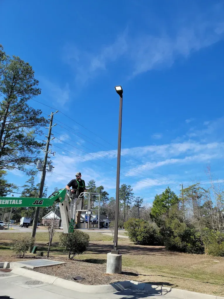 Person on a lift working on a tall light pole against a blue sky.