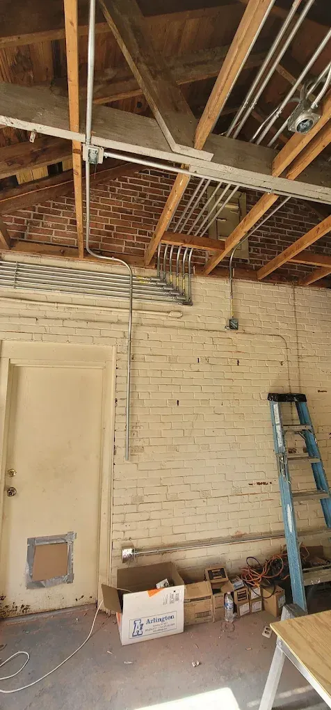 Interior view of a construction site with exposed brick walls, electrical wiring, and a ladder.