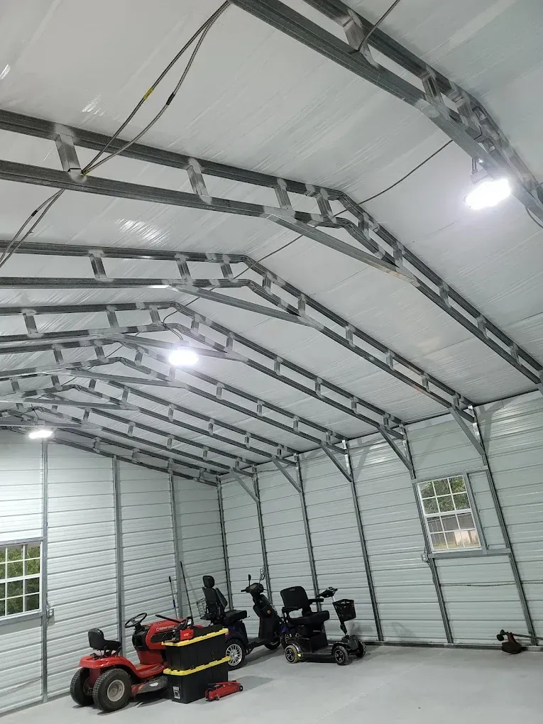 Interior of a metal building with overhead lighting, showing riding lawnmower and mobility scooters.