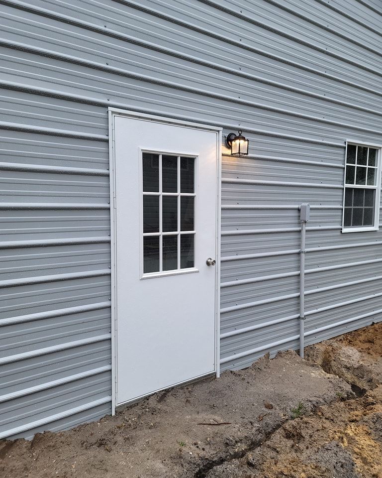 White door with glass panes in a light gray metal-sided building, outdoor setting, small window to the right.