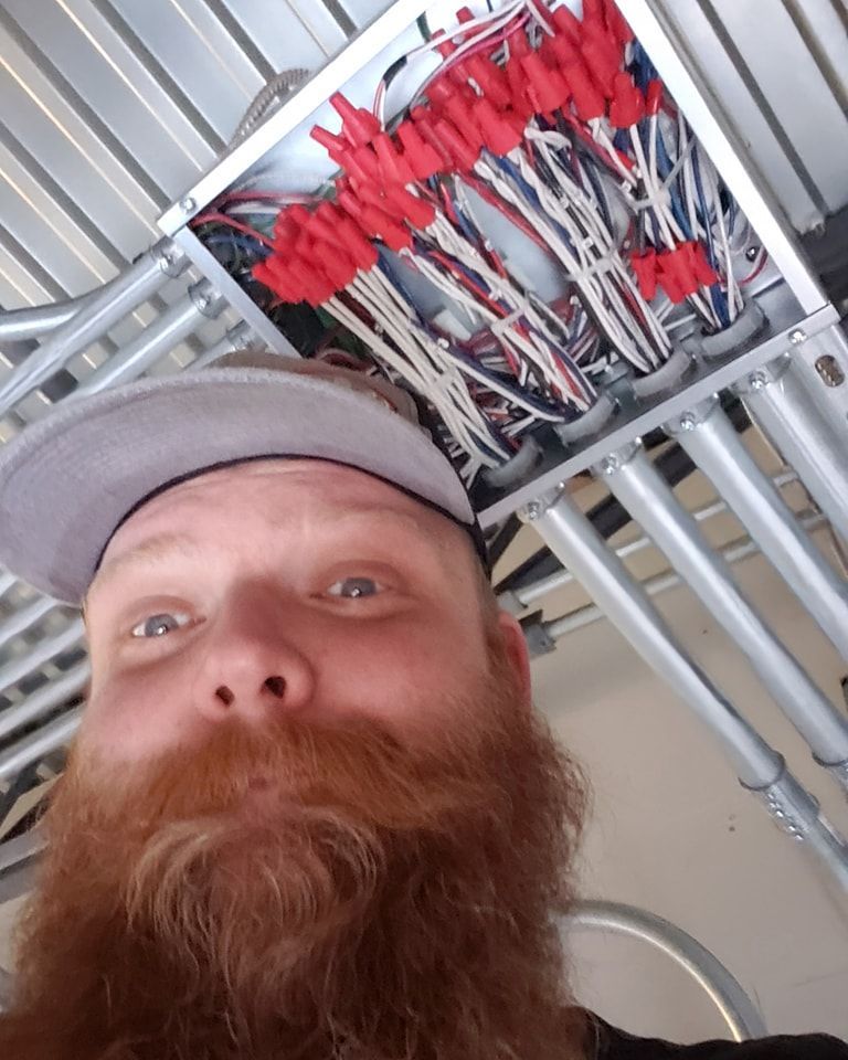 Man with red beard looking up at electrical wiring in a ceiling.