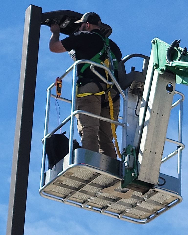 Man in lift basket installing a street light fixture on a dark pole.