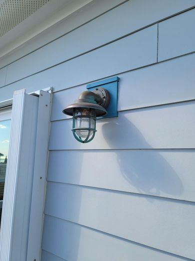 Weathered copper outdoor light fixture mounted on blue wooden panel of white siding.
