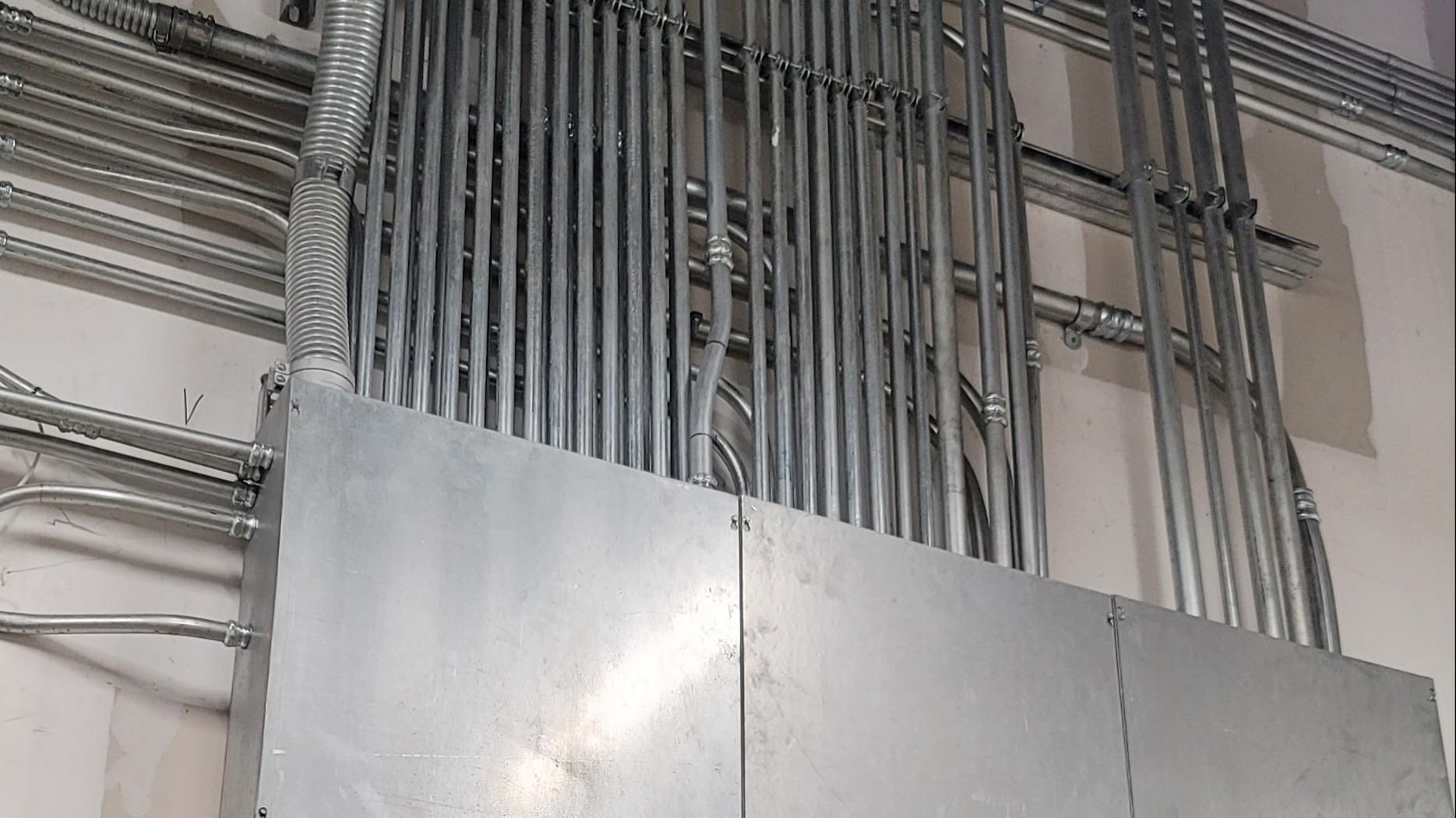 Metal conduit wiring and electrical panel in a construction setting.