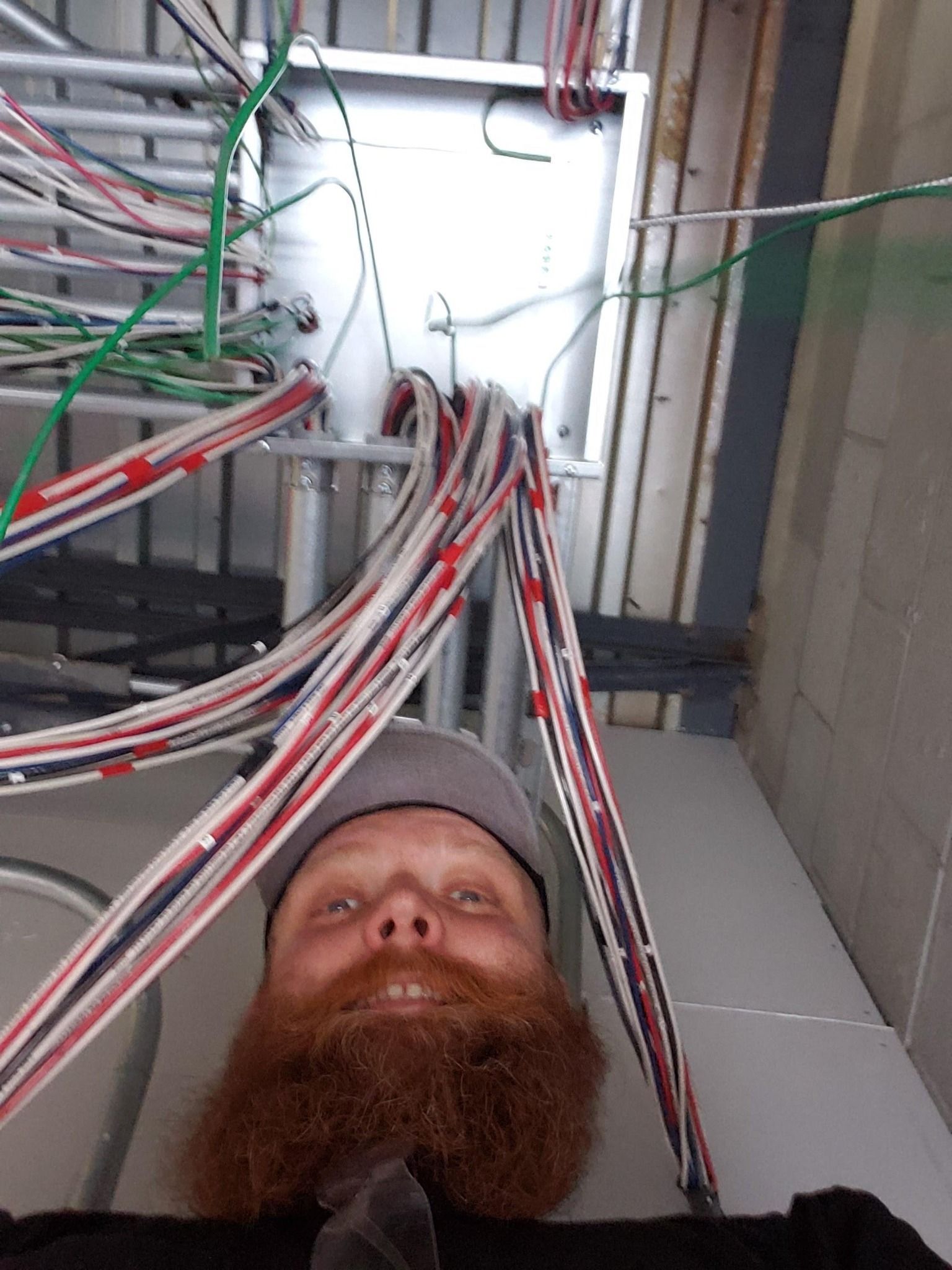 Man with red beard looking up at electrical wiring and metal structure.