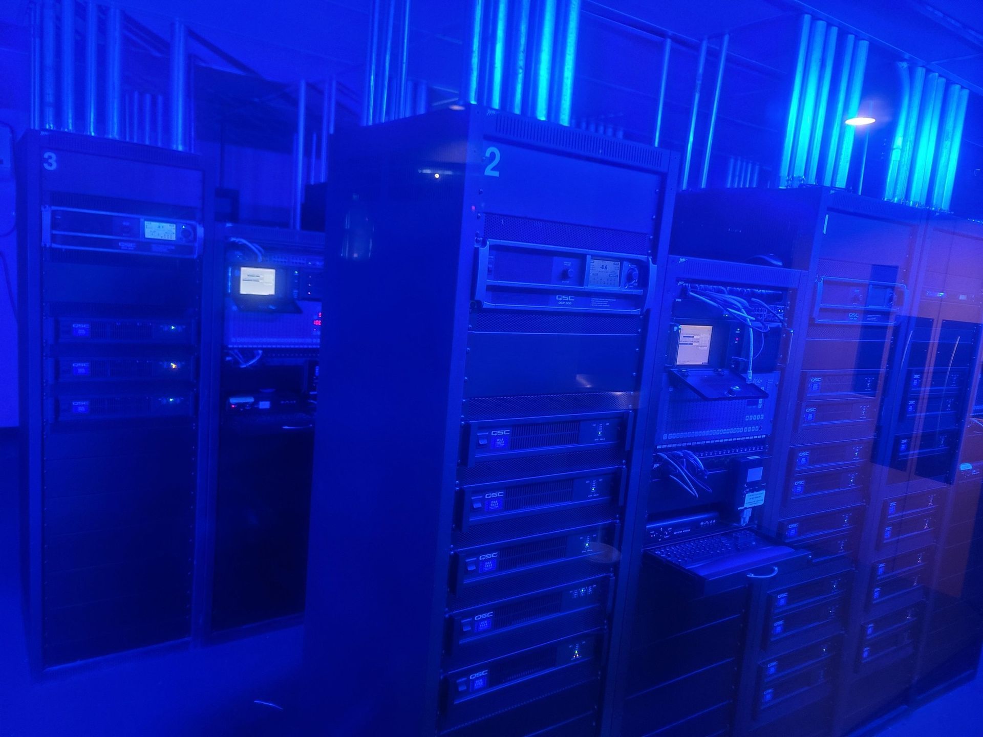 Dark server room with blue lighting. Several tall server racks are arranged in a row.