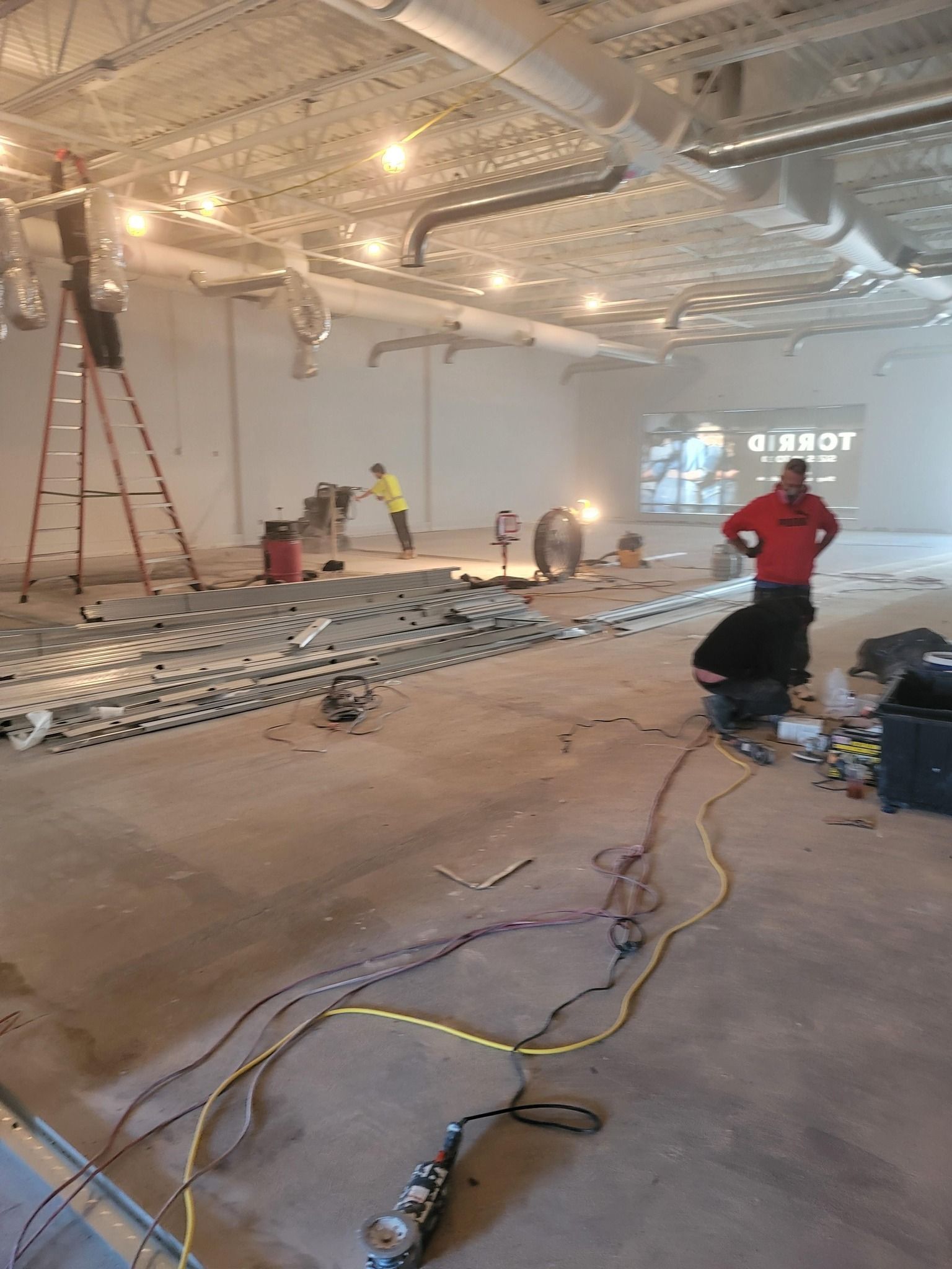 Construction site: Workers inside a large, unfinished space with tools and materials; electrical wiring on the floor.