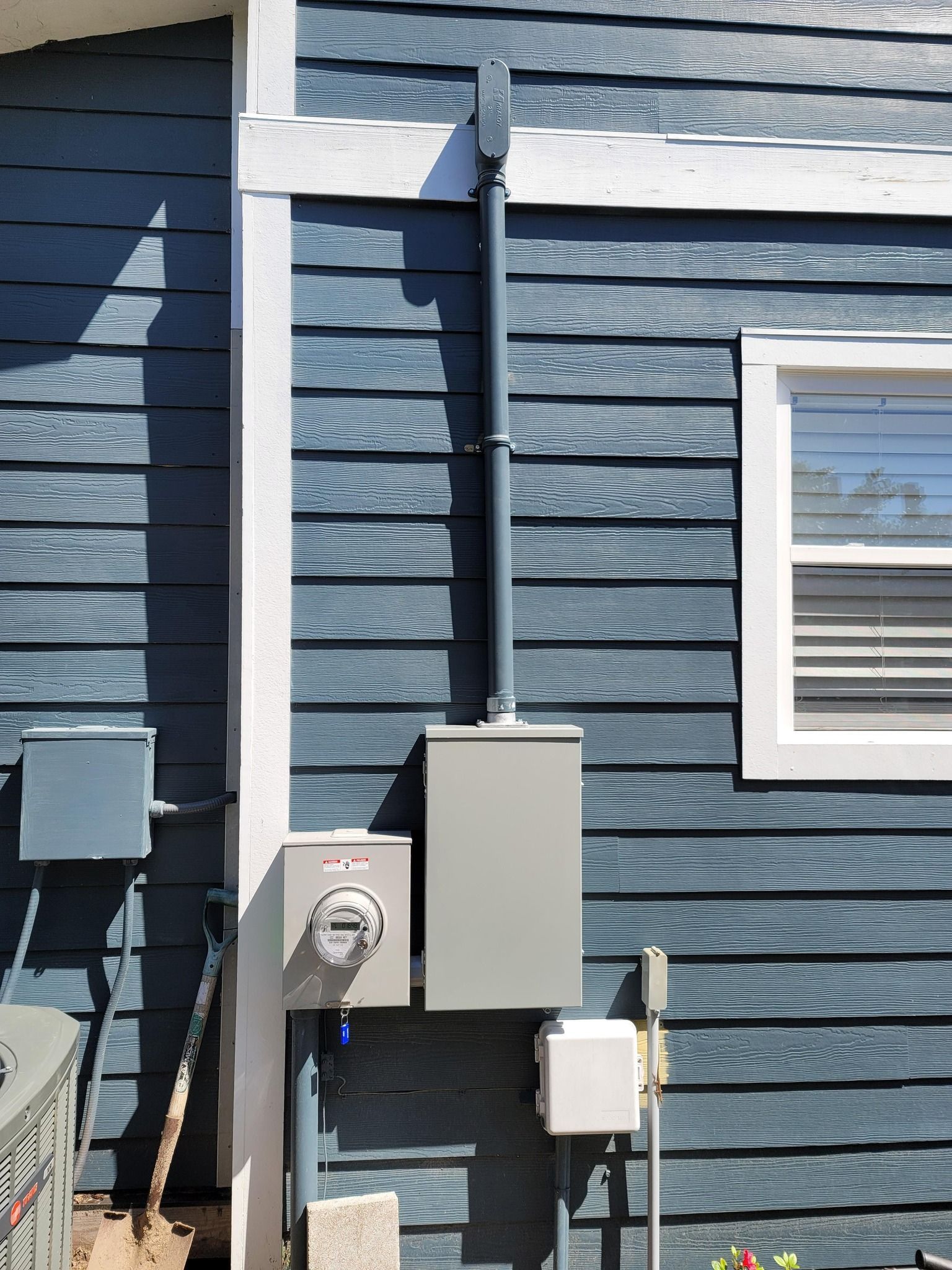 Electrical components mounted on a blue clapboard siding exterior wall. Includes a meter, panel, conduits, and boxes.