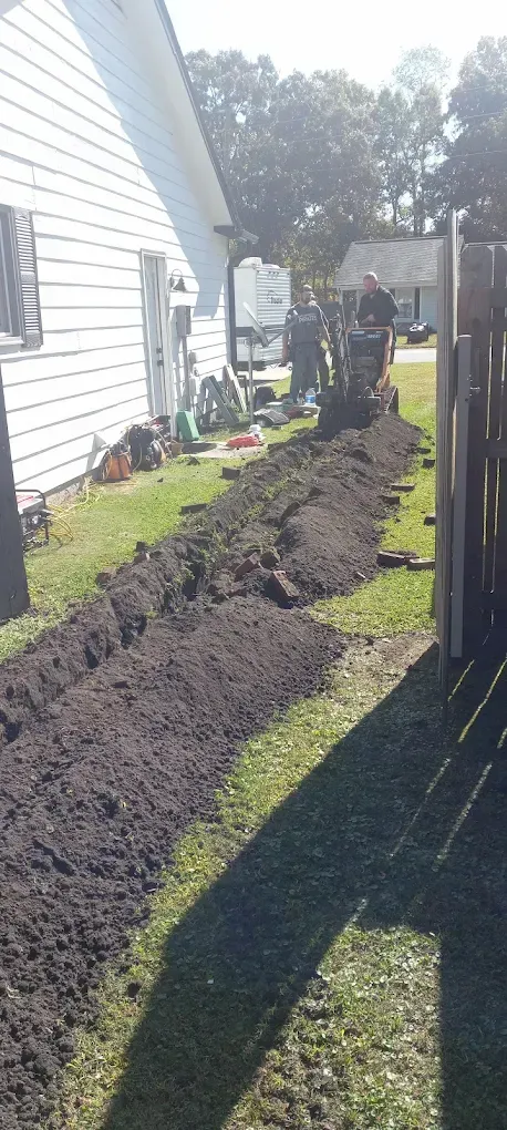 Workers digging a trench in a grassy yard next to a house and a fence.