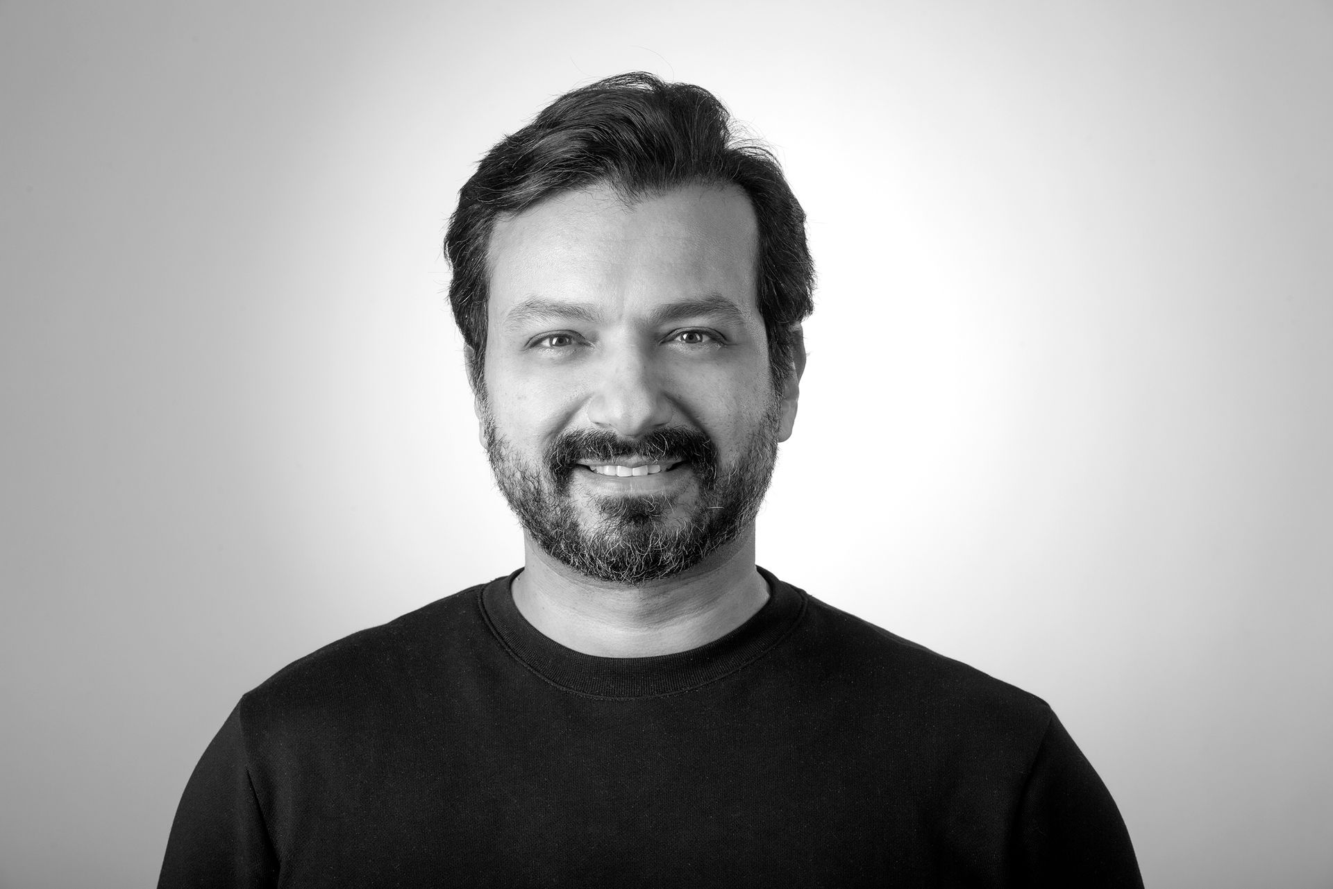 Man with dark hair and beard smiling at the camera, against a light background.