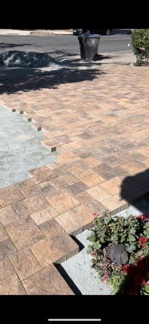 Brick pavers being installed on a driveway, with a small garden area in the foreground.