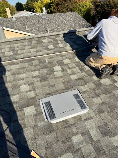 Person working on gray shingle roof, near a vent.
