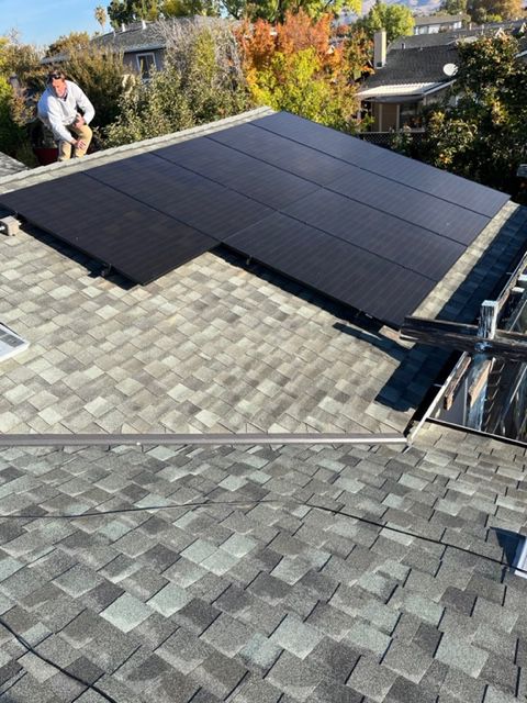 Solar panels installed on a residential roof. A worker is visible, trees in the background.