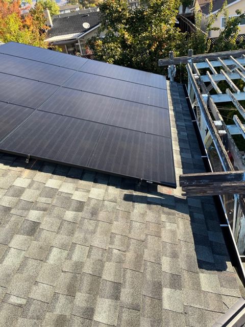 Solar panels installed on a shingled roof next to a partially constructed structure.