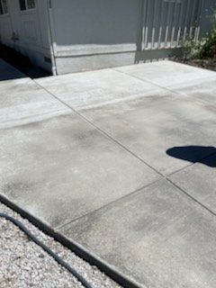 Concrete patio with gray discoloration, next to a building and gravel.