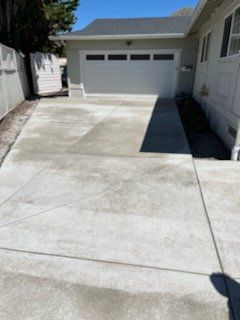 A concrete driveway leading to a garage. The house is light-colored, with a clear sky above.