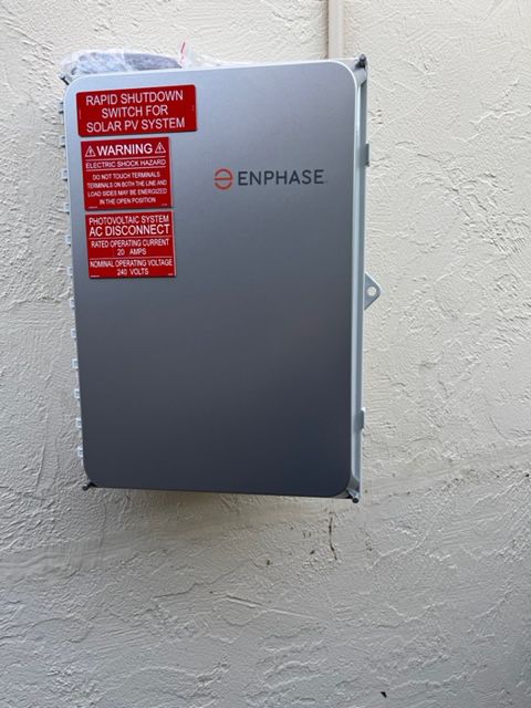 Enphase solar power system electrical box mounted on a white wall, with warning labels.