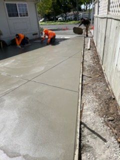 Workers in orange vests finishing a concrete sidewalk. Gray concrete, sunny day.