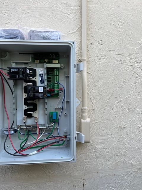 Open gray electrical box on a beige wall, with wires, circuit breakers, and electronic components.