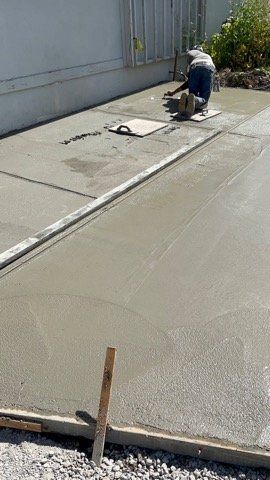 Person smoothing wet concrete on a sidewalk with a power tool near a building.