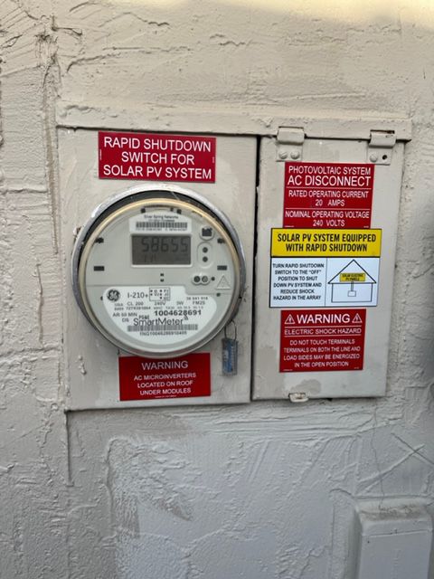 Electric meter and AC disconnect box on a wall, labeled for solar PV system rapid shutdown.
