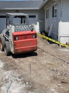 Bobcat on a dirt driveway next to a house with caution tape blocking an area.